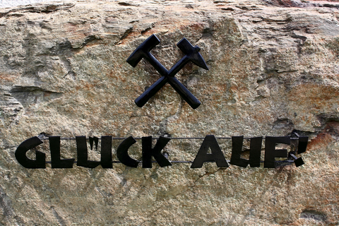 Foto: Schwarzer Schriftzug "Glück Auf" und Eisen und Schlägel Symbolik auf hellgrauem Stein.