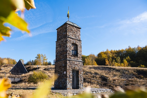 Foto: Ein gemauerter Turm mit Eisentor vor Haldengelände und blauem Himmel. Auf dem Turm ist ein Wimpel in gelb-schwarz angebracht. Im Vordergrund des Bildes befindet sich am unteren und linken Bildrand unscharf erfasstes Herbstlaub.